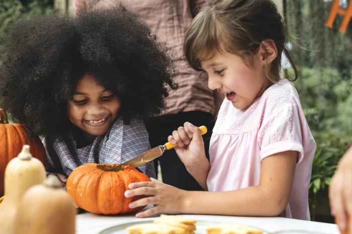 Children using a butter knife to safely carve a pumpkin.